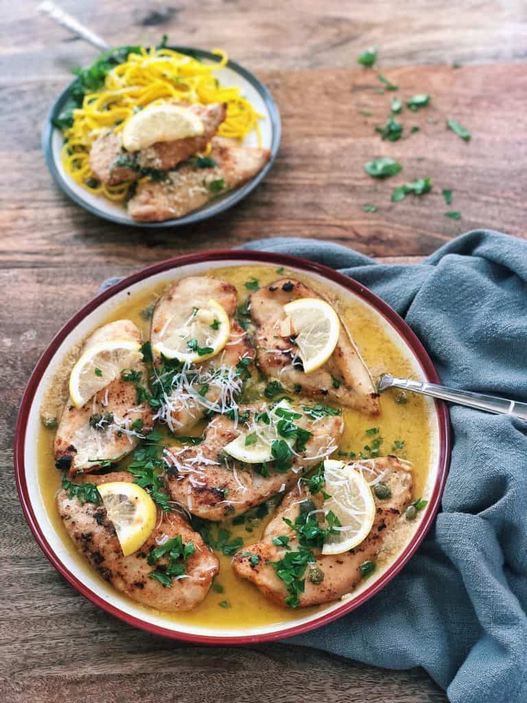 Chicken piccata in a plate with lemon and parsley and noodles