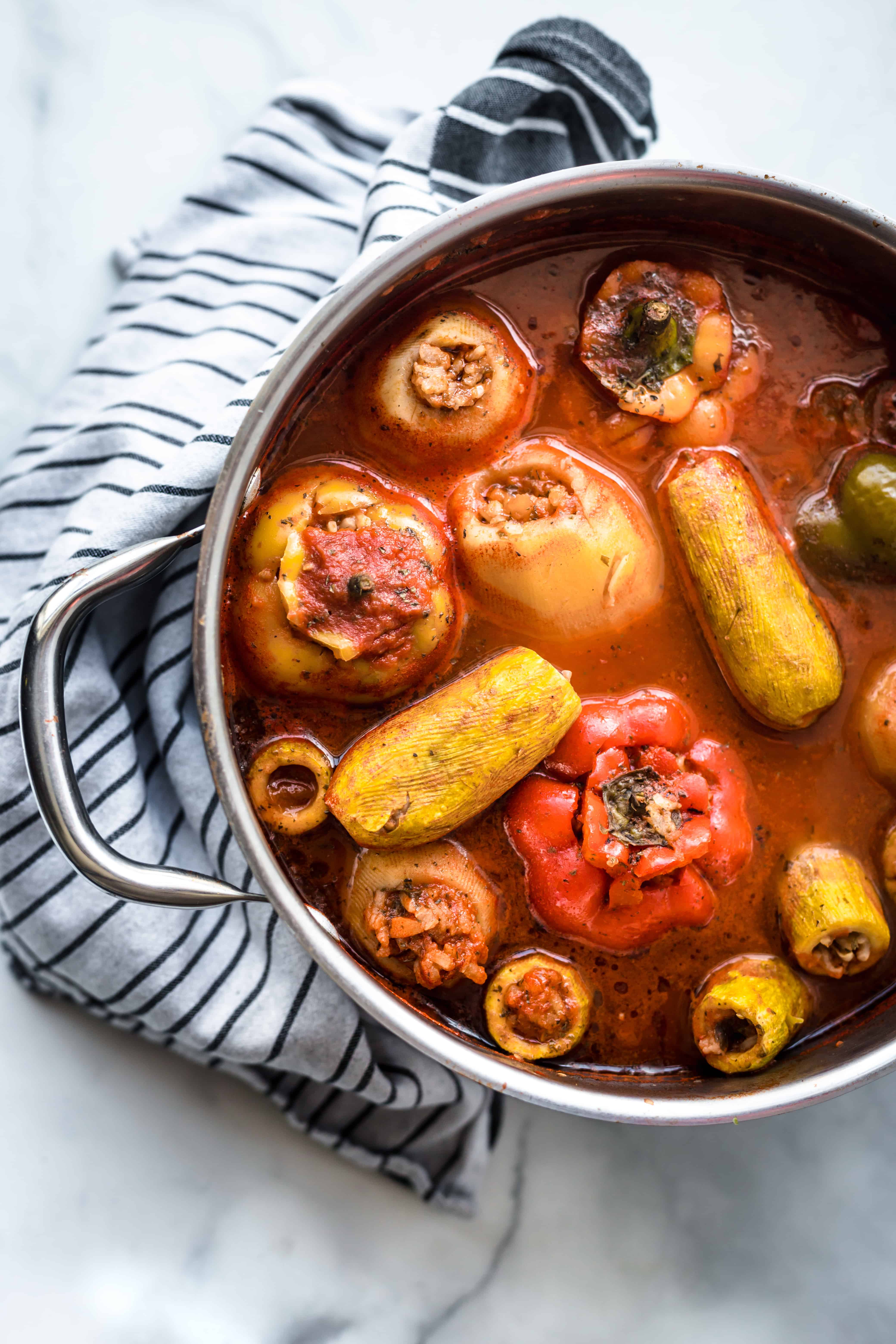 Stuffed vegetables in tomato broth in a large saucepan with a kitchen towel under the pan