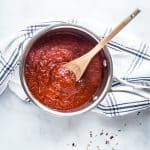pizza sauce in a pan with a wooden spoon on a white kitchen towel