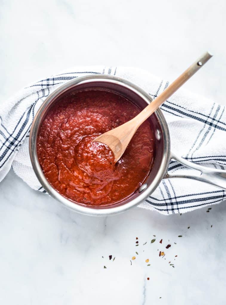 pizza sauce in a pan with a wooden spoon on a white kitchen towel
