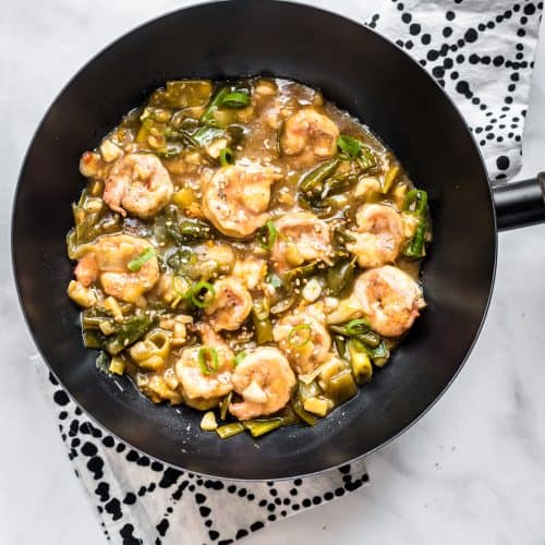 A skillet filled with honey garlic prawns over a patterned kitchen towel