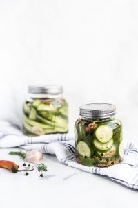 two jars full of dill pickles on a white kitchen towel