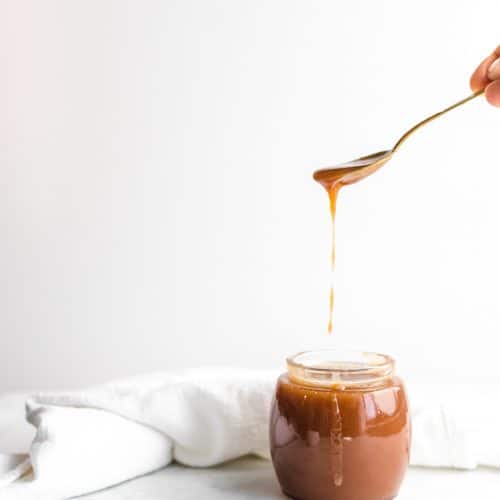 Jar of rose water and orange blossom water salted caramel sauce with a spoon dripping some salted caramel off of it