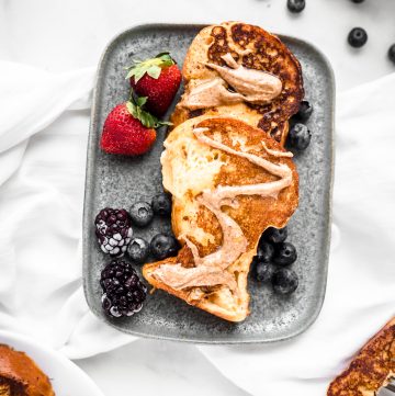 Brioche french toast on a gray plate over a white kitchen cloth with almond butter drizzle