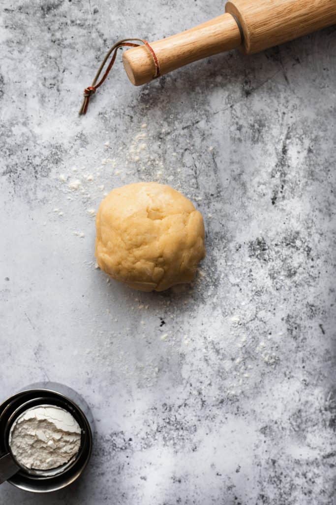 Ball of easy pie dough with a rolling pin and a measuring cup full of flour
