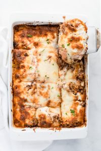 Lasagna slice being lifted out of a whole lasagna on a white baking dish