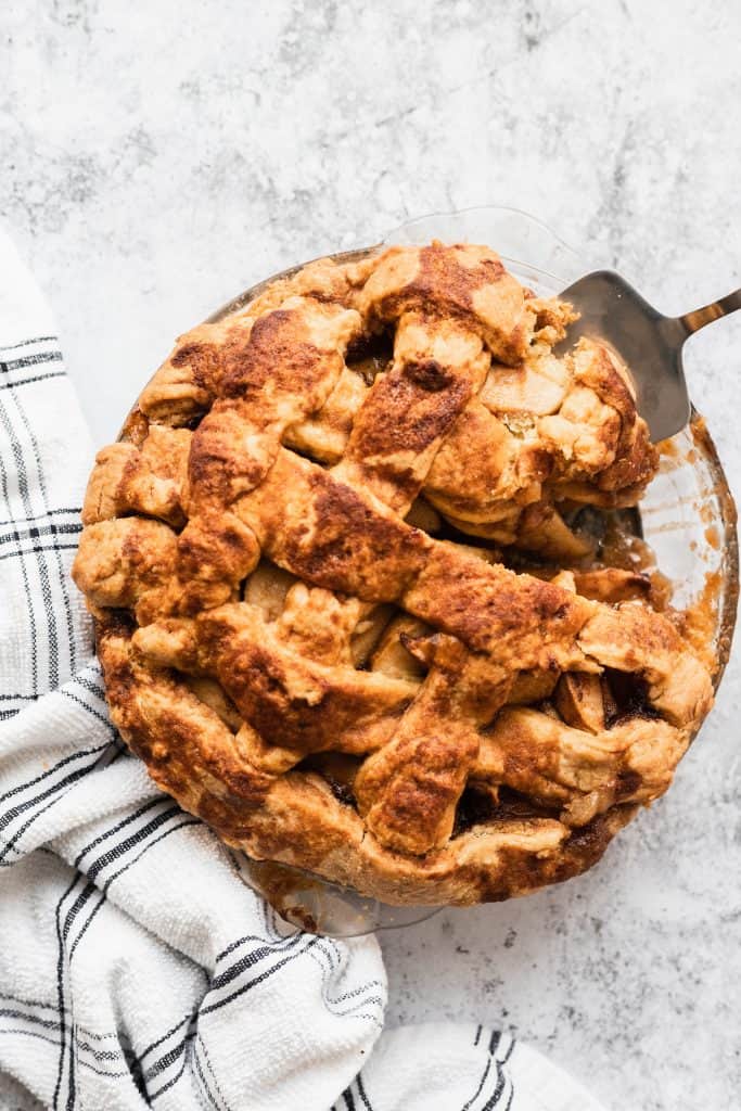 Easy apple pie in a glass pie plate with a slice being lifted out