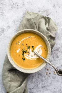Bowl of pumpkin curry soup with a spoon in it on a kitchen towel