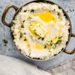Roasted garlic mashed cauliflower in a bowl with a kitchen towel and roasted garlic cloves