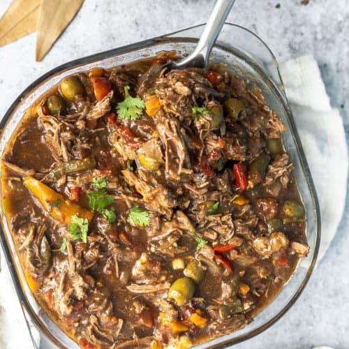 Big bowl of ropa vieja shredded beef with olives and bay leaves on the side