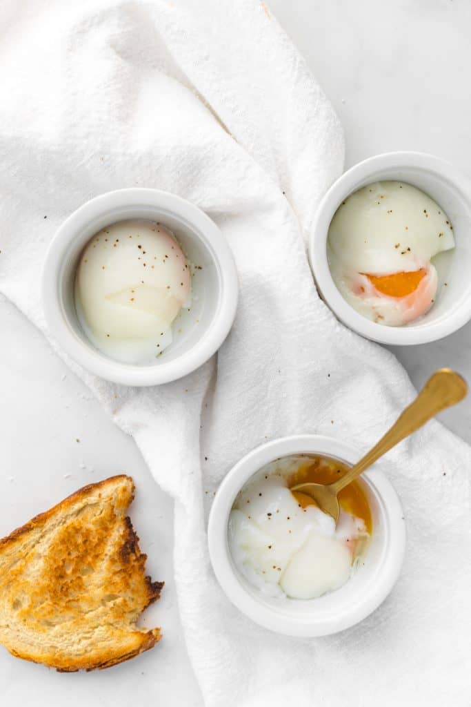 Three sous vide eggs in ramekins with a piece of bread