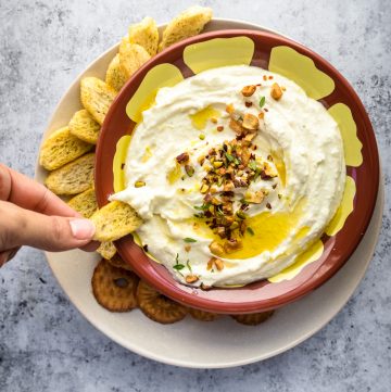 Greek Feta dip in a bowl with some being scooped out by a hand