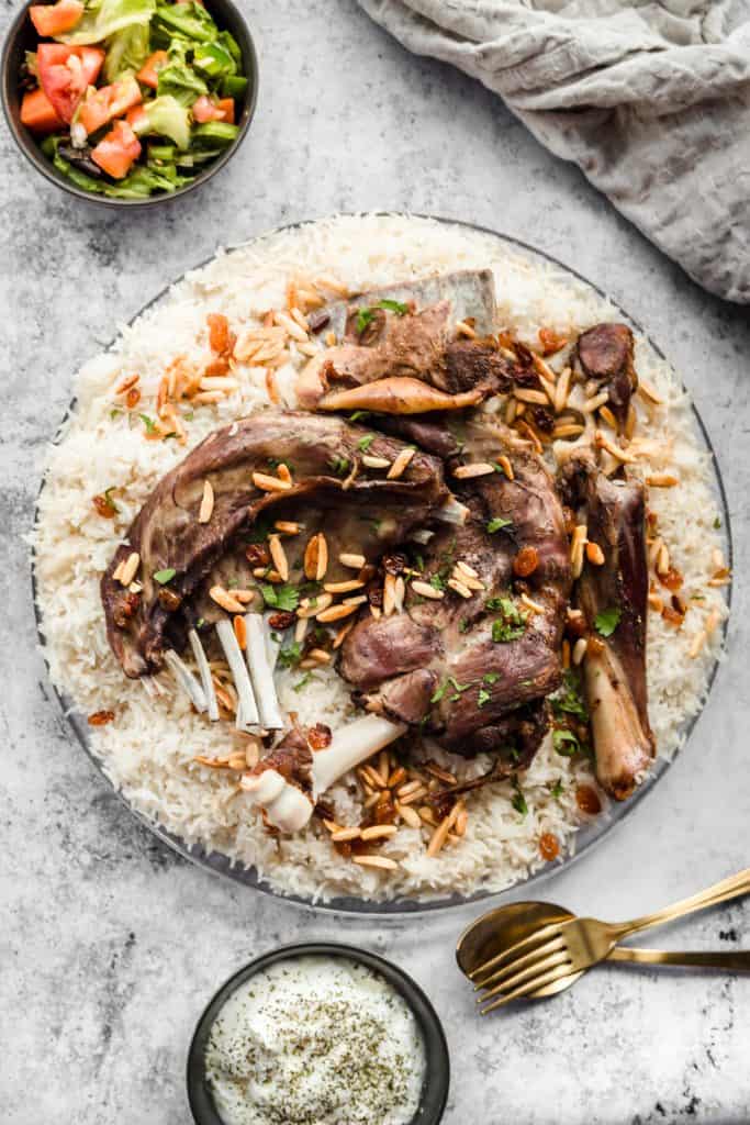 Lamb mandi on top of rice with toasted nut with cucumber yogurt and utensils