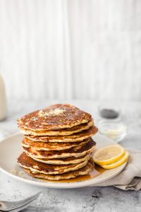 stack of lemon poppyseed pancakes on a plate with lemon slices and a kitchen towel