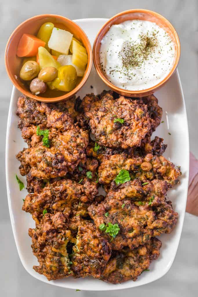 A platter full of fritters with parsley on top, yogurt on the side
