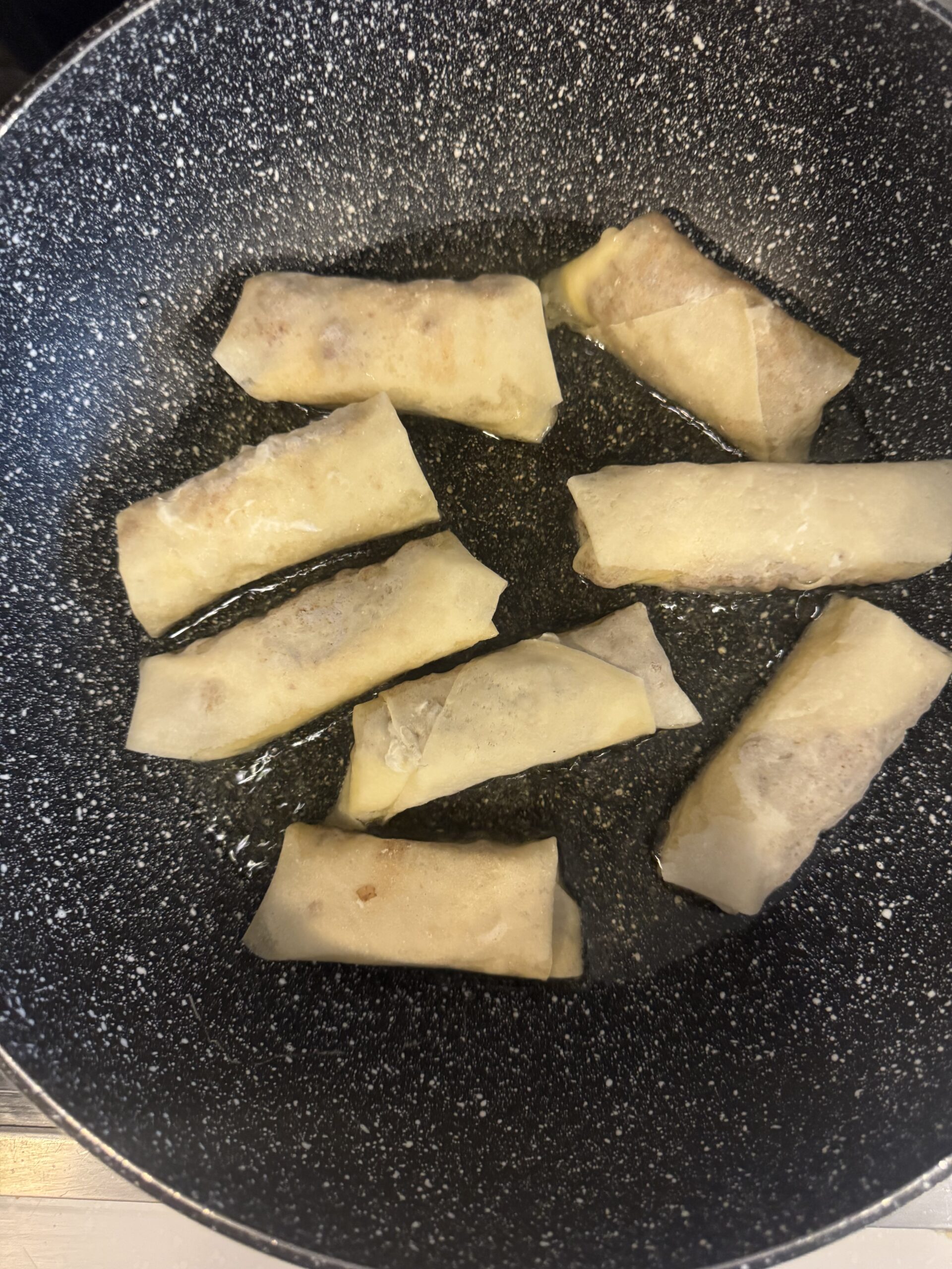 Spring rolls placed in hot oil in a large skillet.