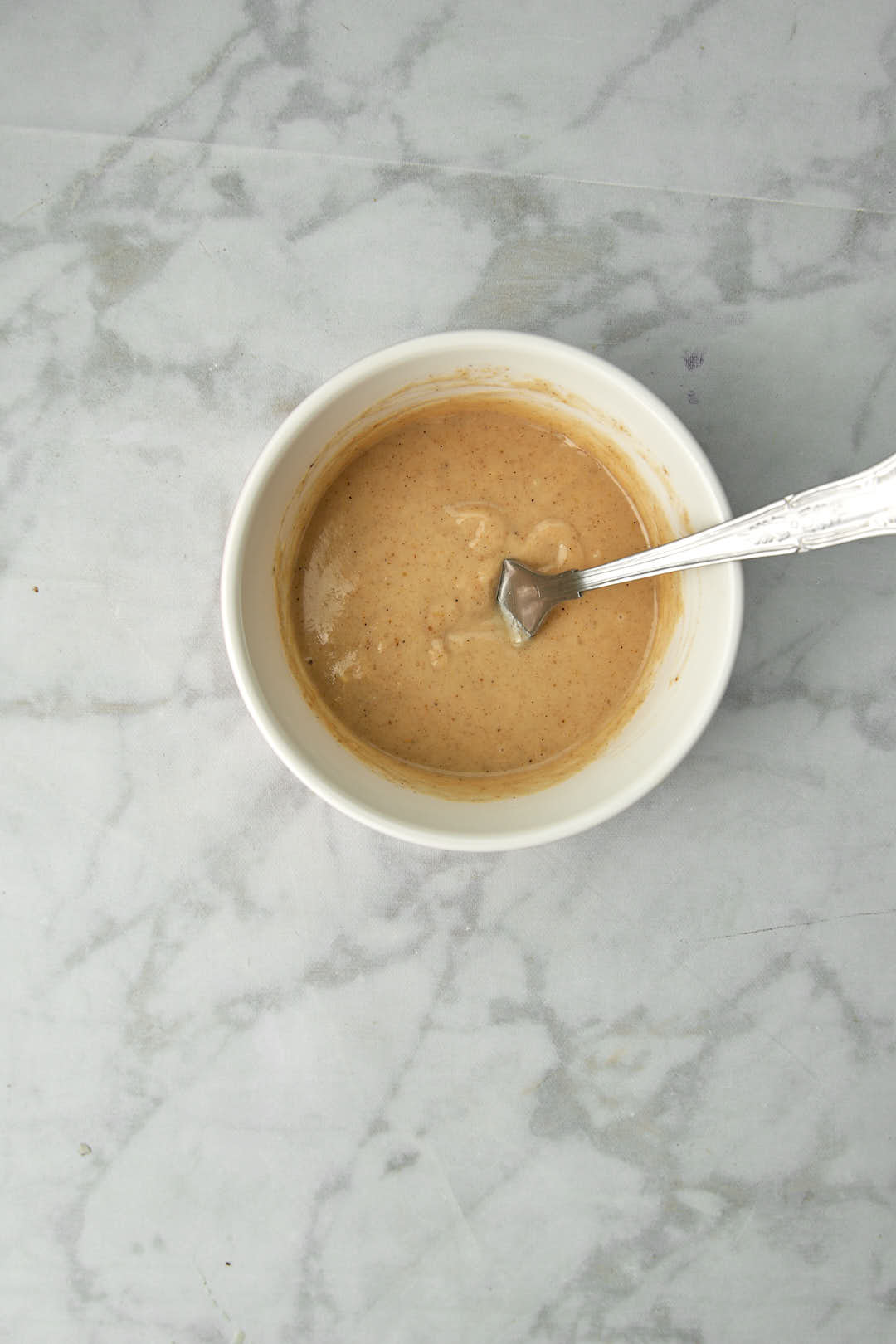 tahini dressing in a white bowl with a fork in it.