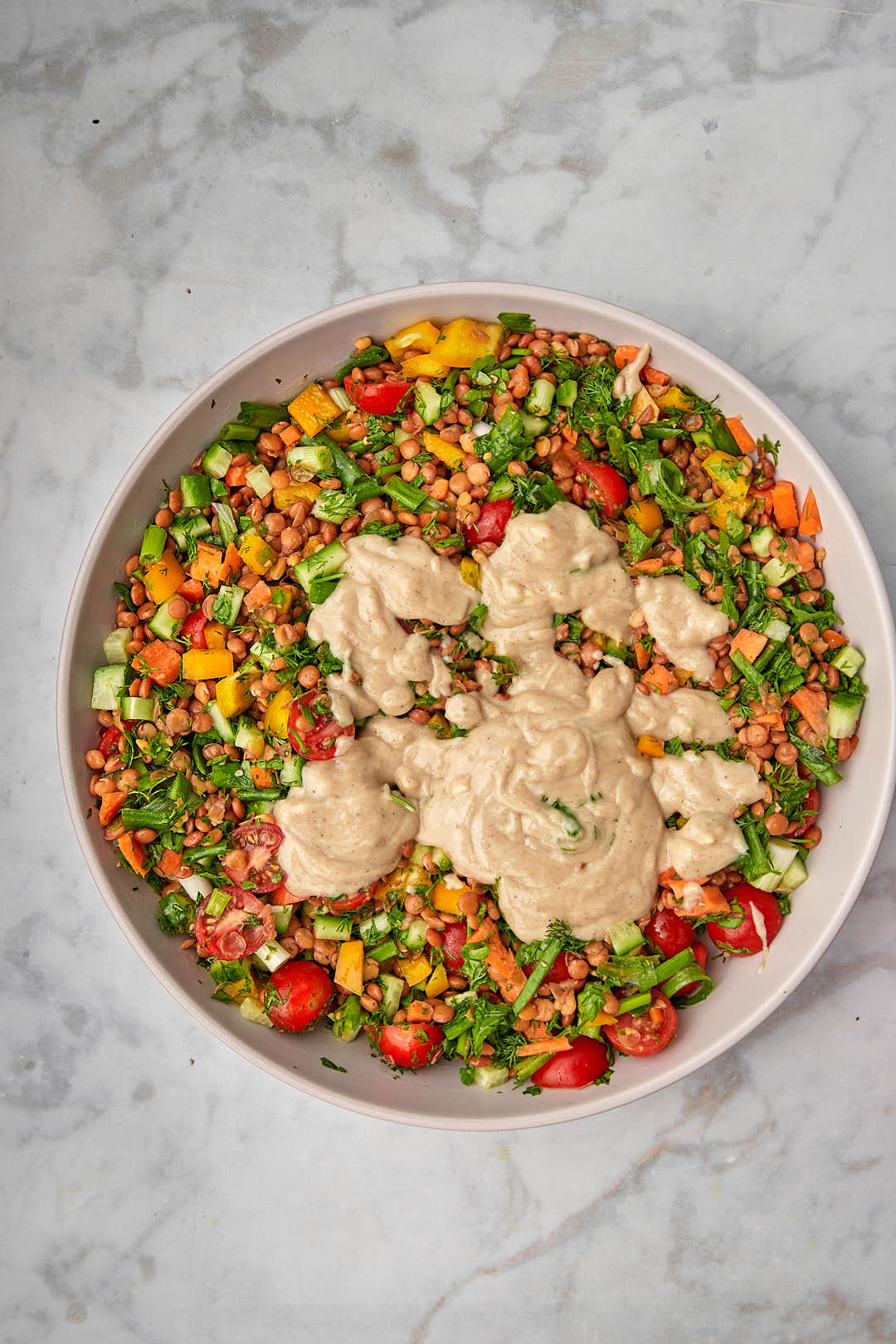 Tahini dressing drizzled onto lentil salad ingredients