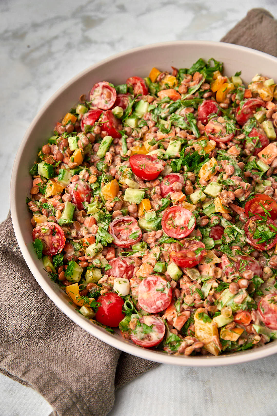 Lentil salad with tahini dressing on dark kitchen towel on marble background.