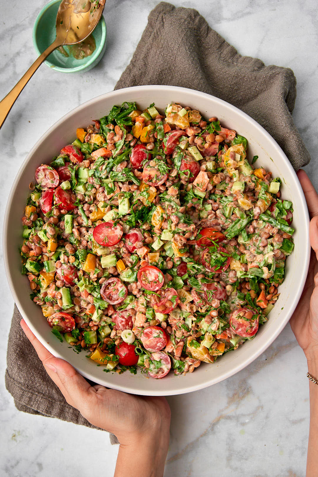 Hands holding a platter of vegan lentil salad with tahini dressing.