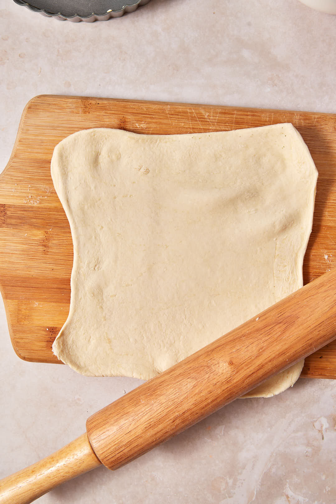 puff pastry rolled out on a wooden board with a rolling pin.