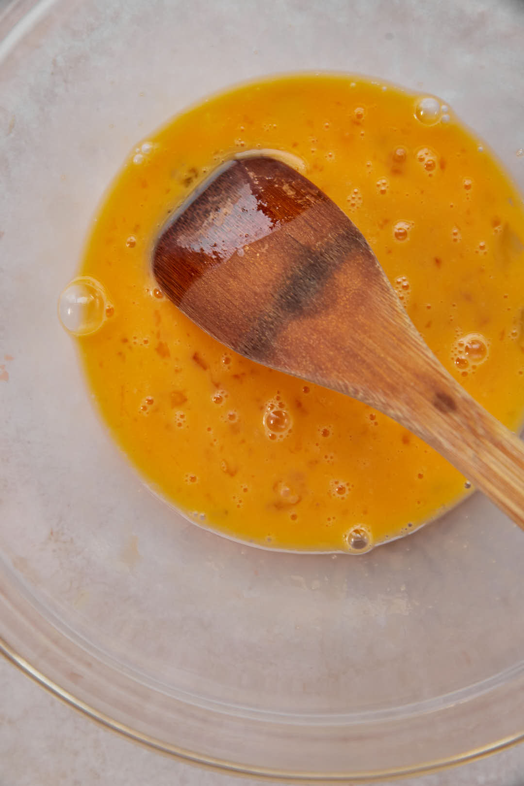 Beaten eggs in a glass bowl with a wooden spoon.