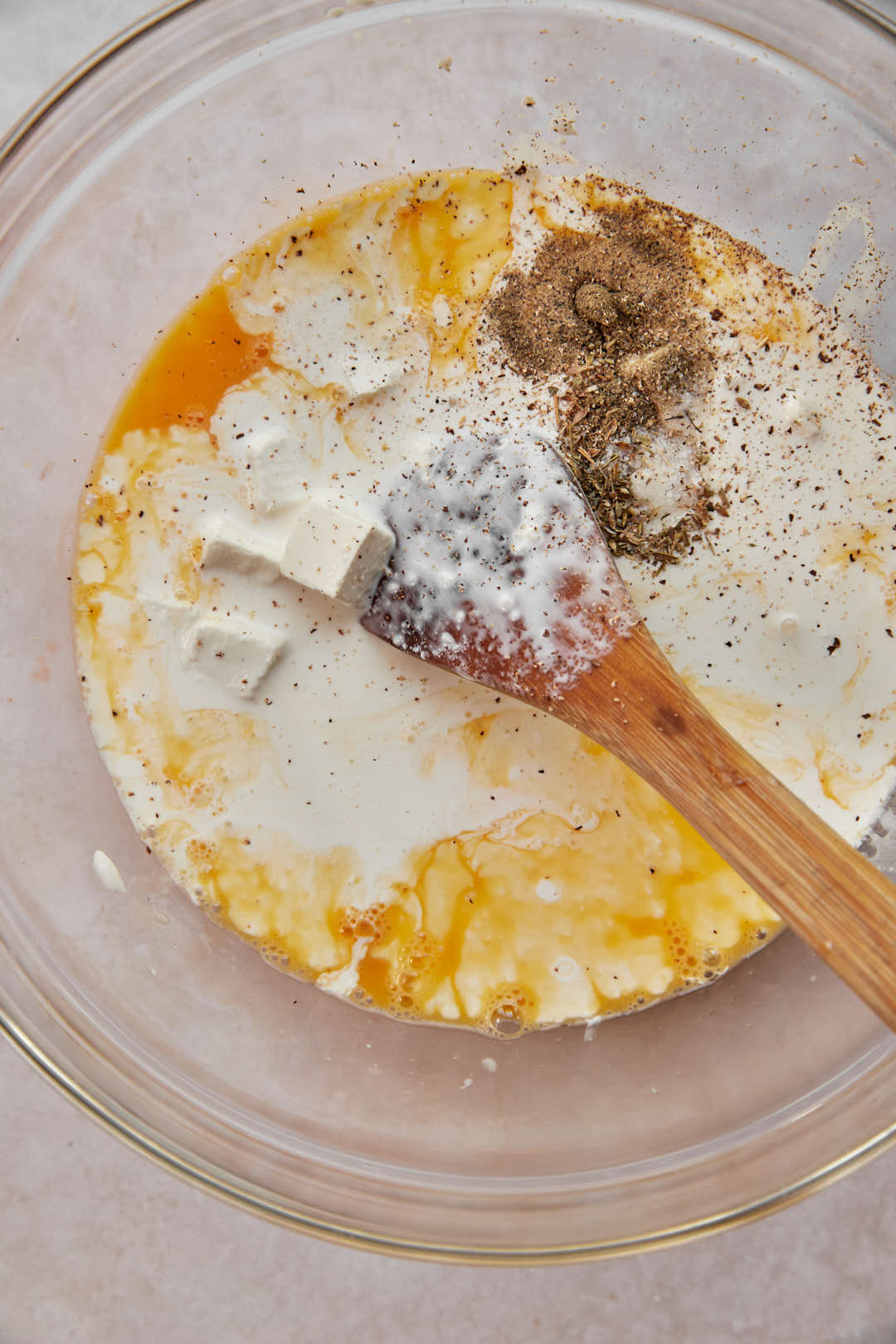 Cream, feta cheese and seasonings in eggs in a glass bowl.