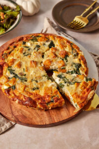 a pumpkin and feta quiche on a serving platter with a slice being taken out with a golden cake server.