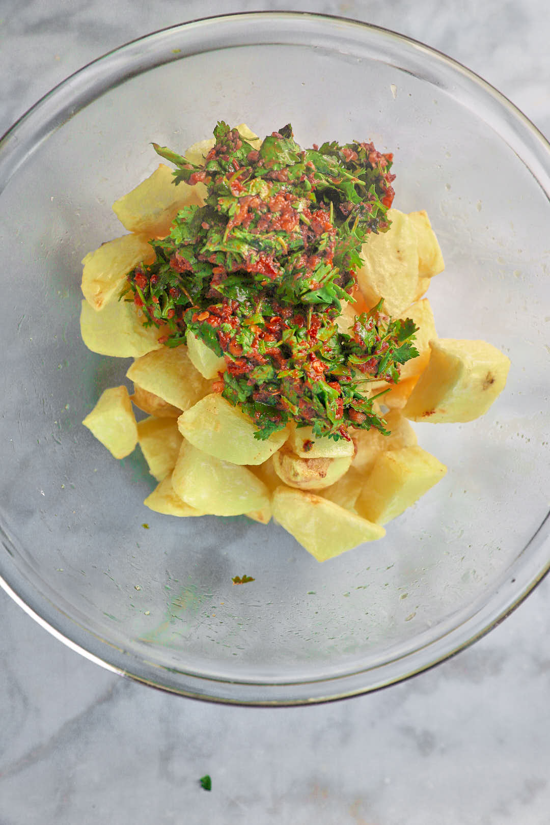 Red pepper paste on cooked potato cubes in glass bowl.