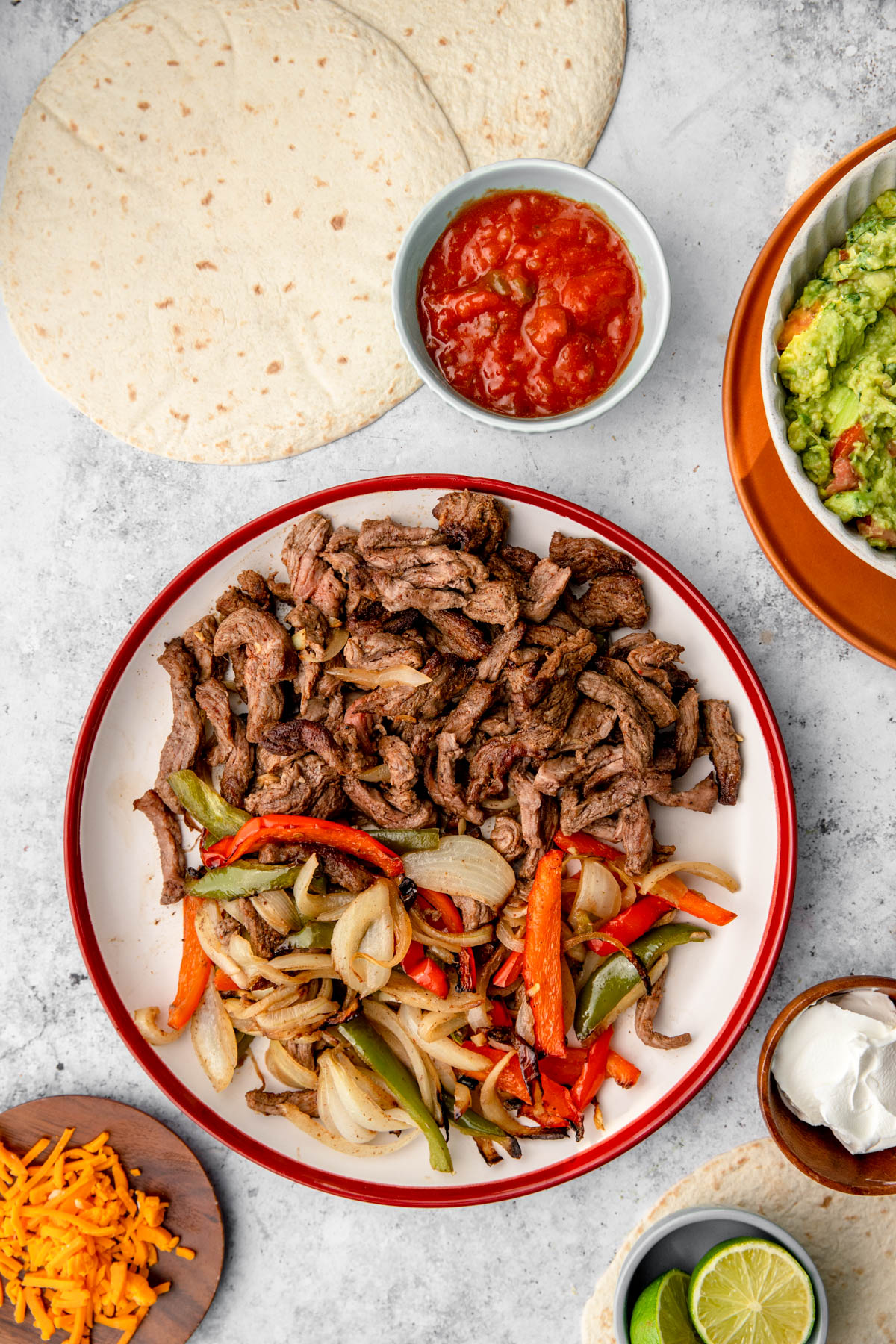 air fryer steak fajitas on a plate with guacamole, cheese and sour cream on side