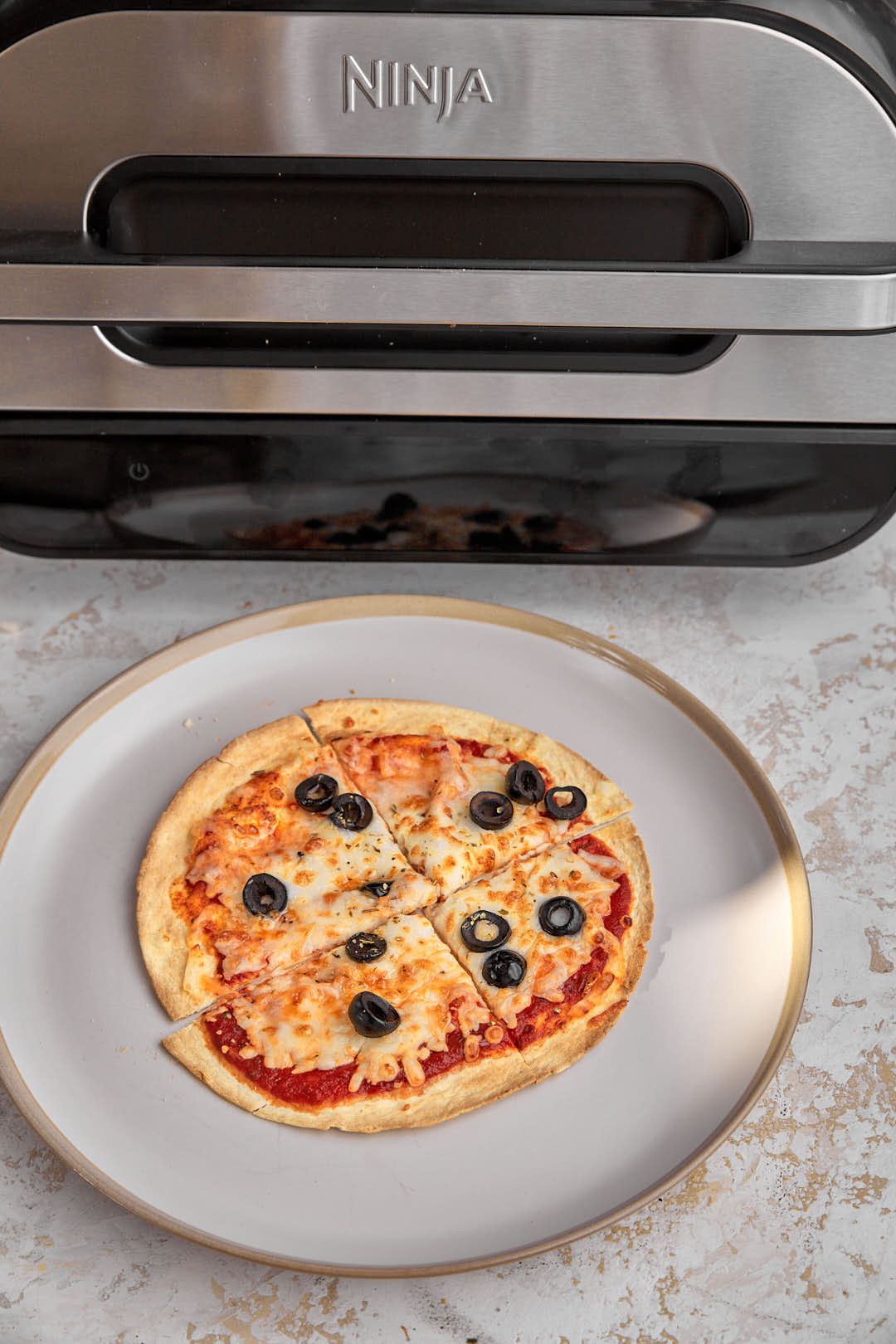 air fryer tortilla pizza on a white plate in front of an air fryer machine.