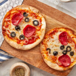 two air fryer tortilla pizzas with pepperoni and sliced black olives on a wooden cutting board.