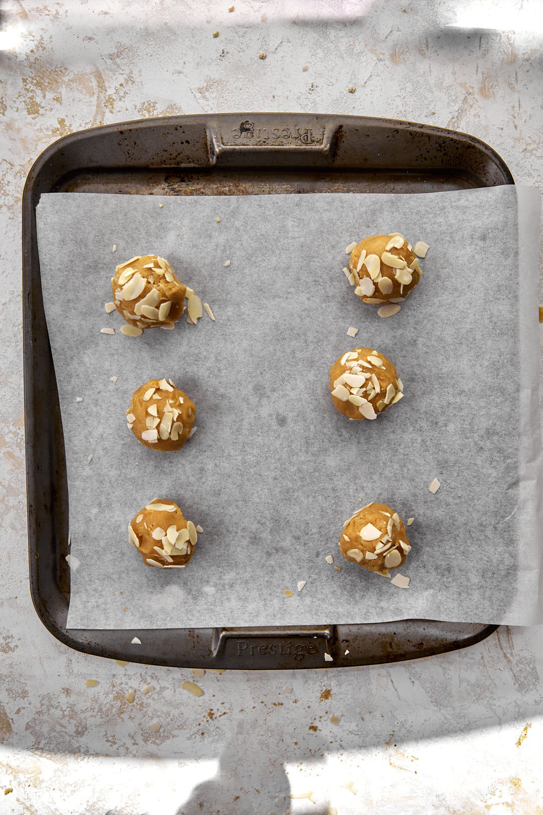 cookie dough balls rolled in almond flakes on parchment paper lined baking sheet.