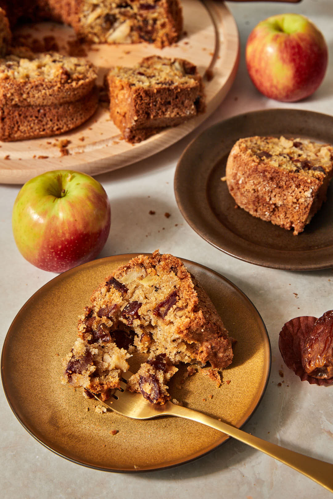slice of apple date cake on a brown plate with a gold fork taking a bite out of it.
