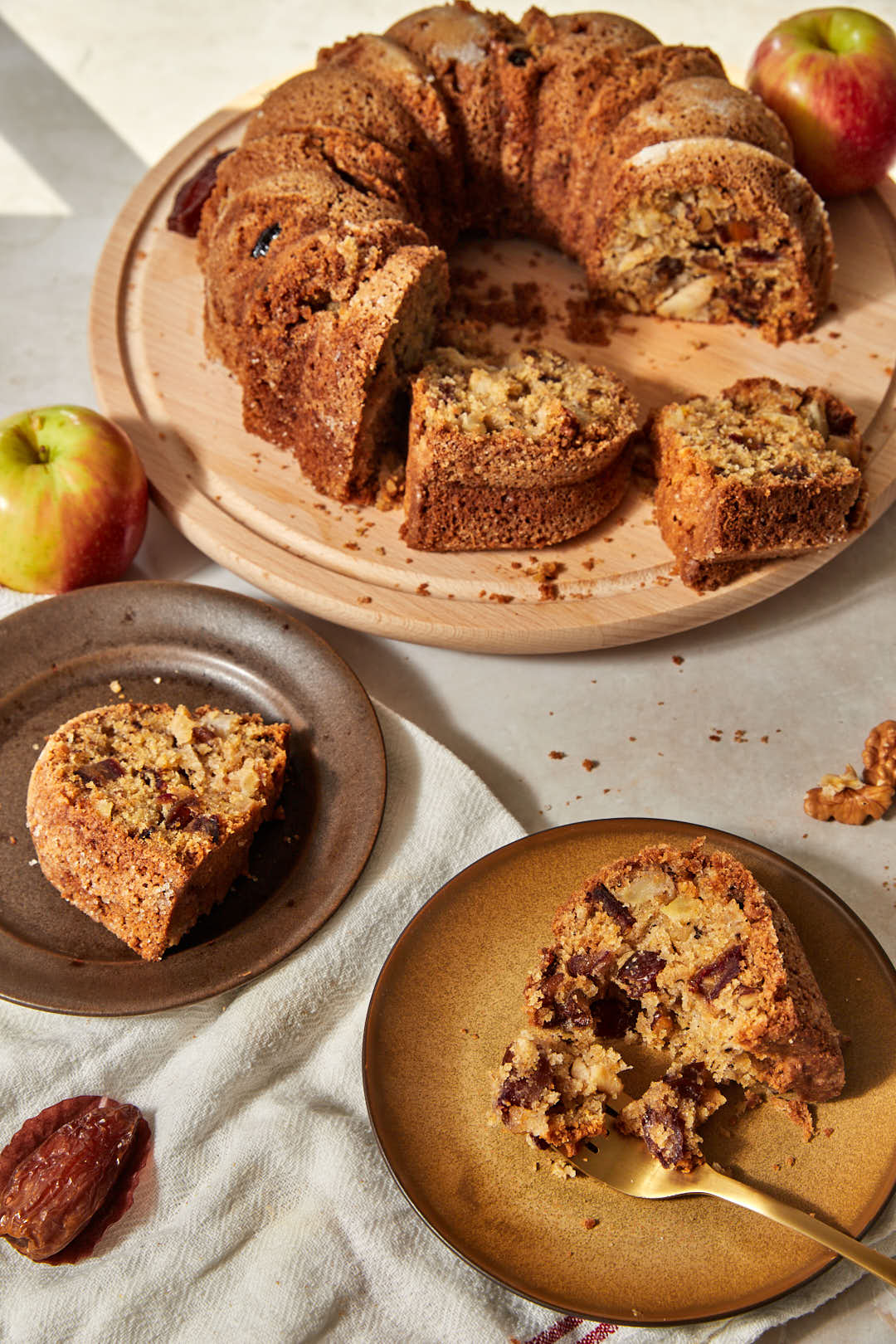 apple walnut date bundt cake on a wooden platter with two slices of cake on brown plates.