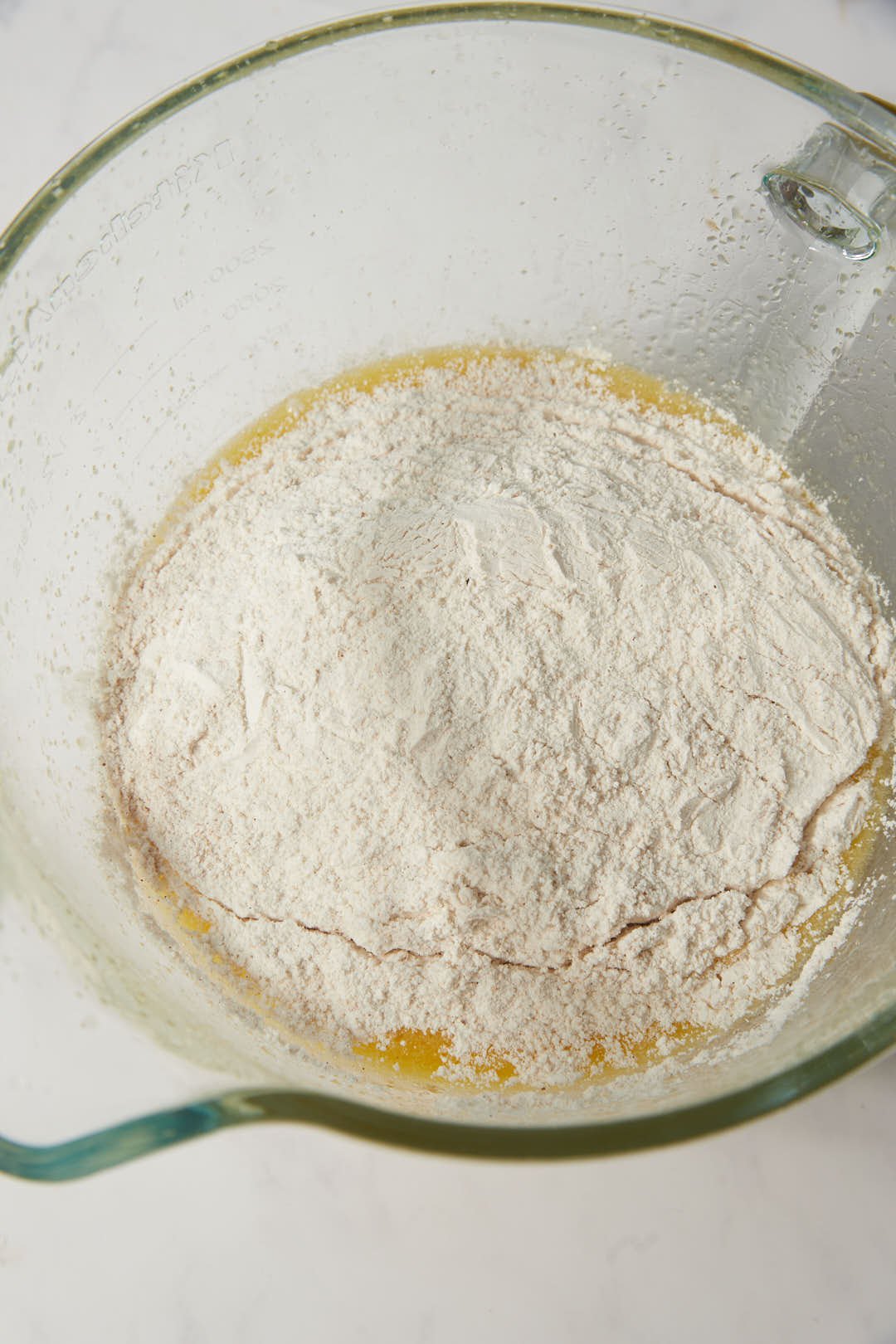 dry ingredient sfor apple cake added to wet ingredients in a glass bowl.