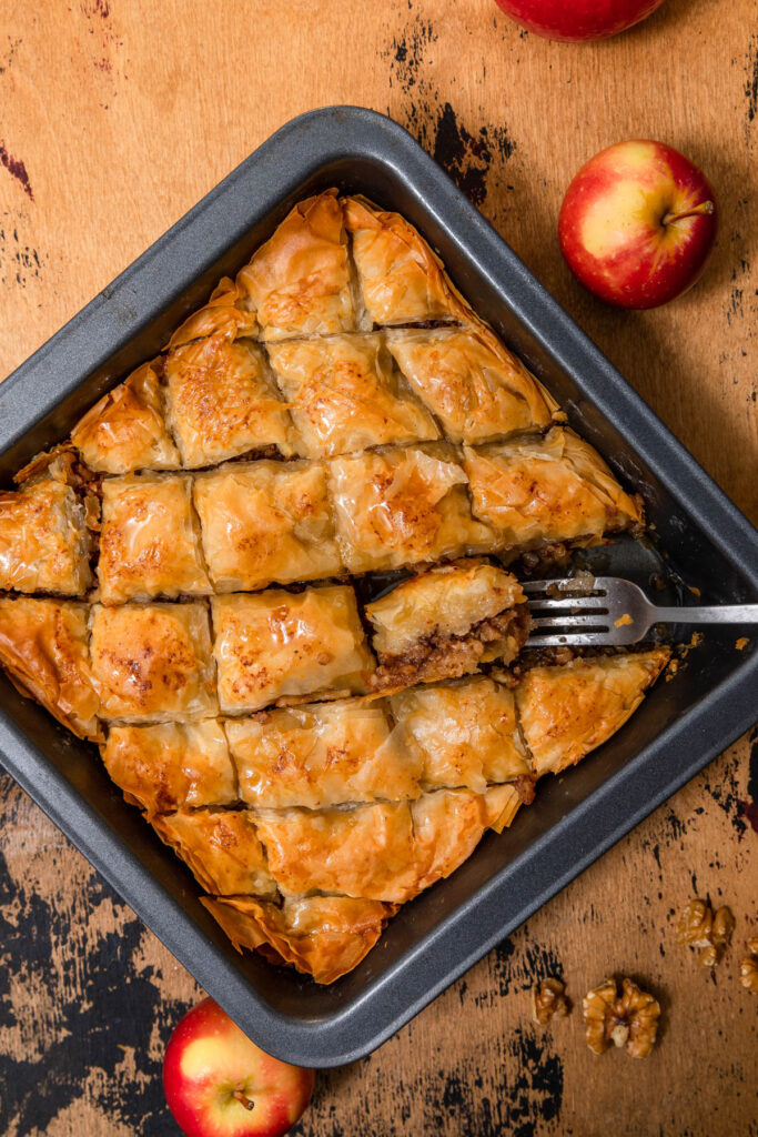 apple baklava in square pan with extra apples and a knife on the side.
