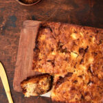 Apple yogurt cake on cutting board with milk in the background.