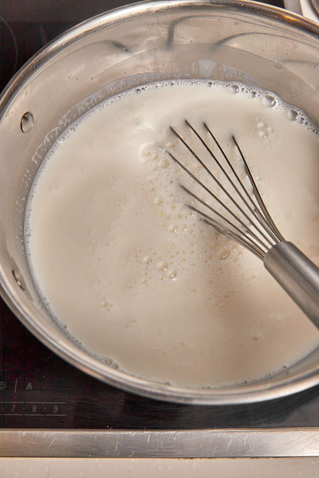 a large saucepan filled with milk with a wire whisk in it.