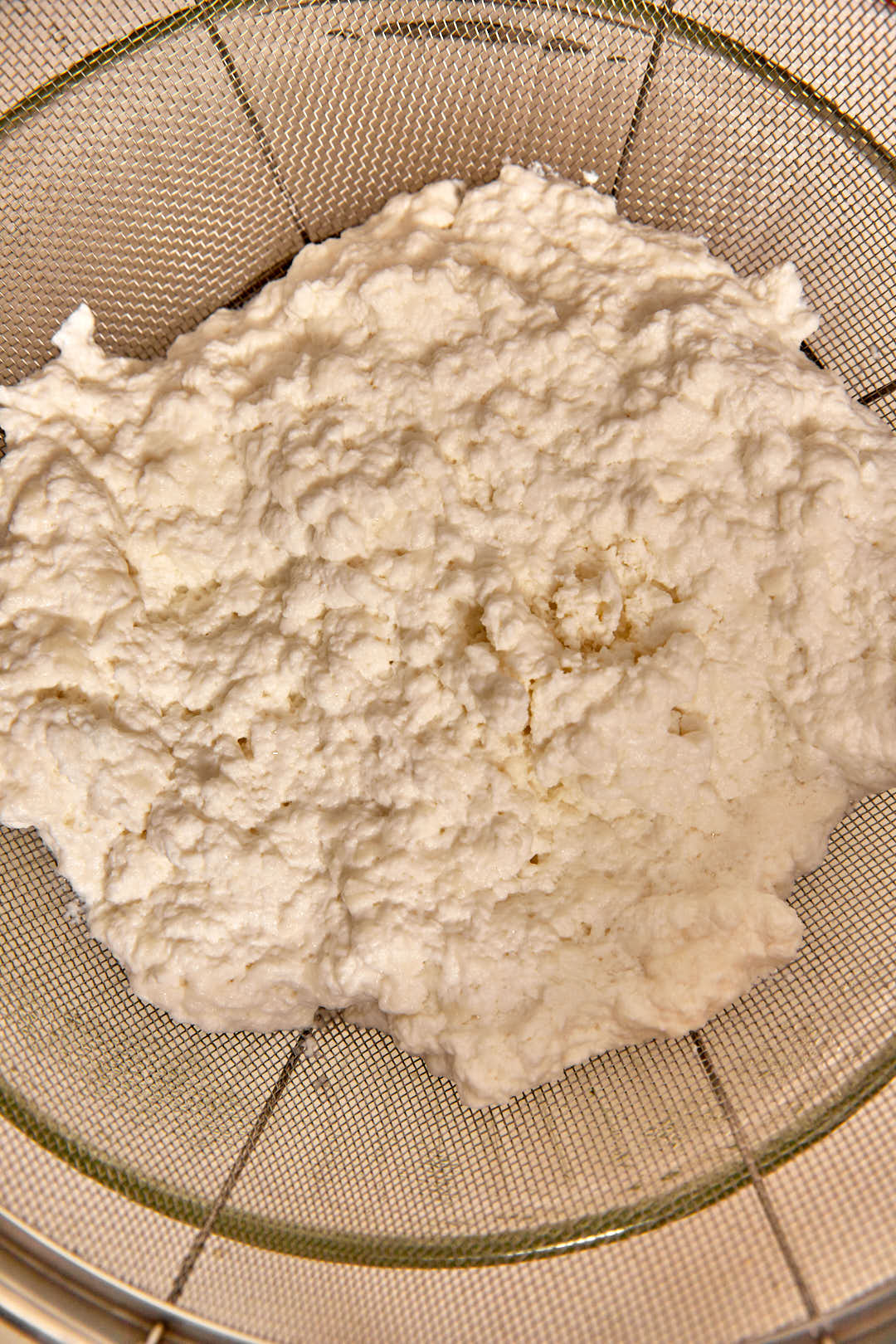 milk curds in a strainer set over a bowl.
