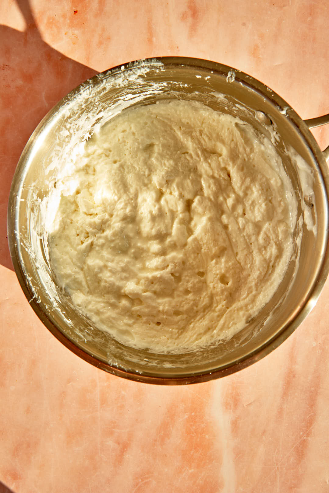 Chilled ashta in a saucepan set on a pink background.