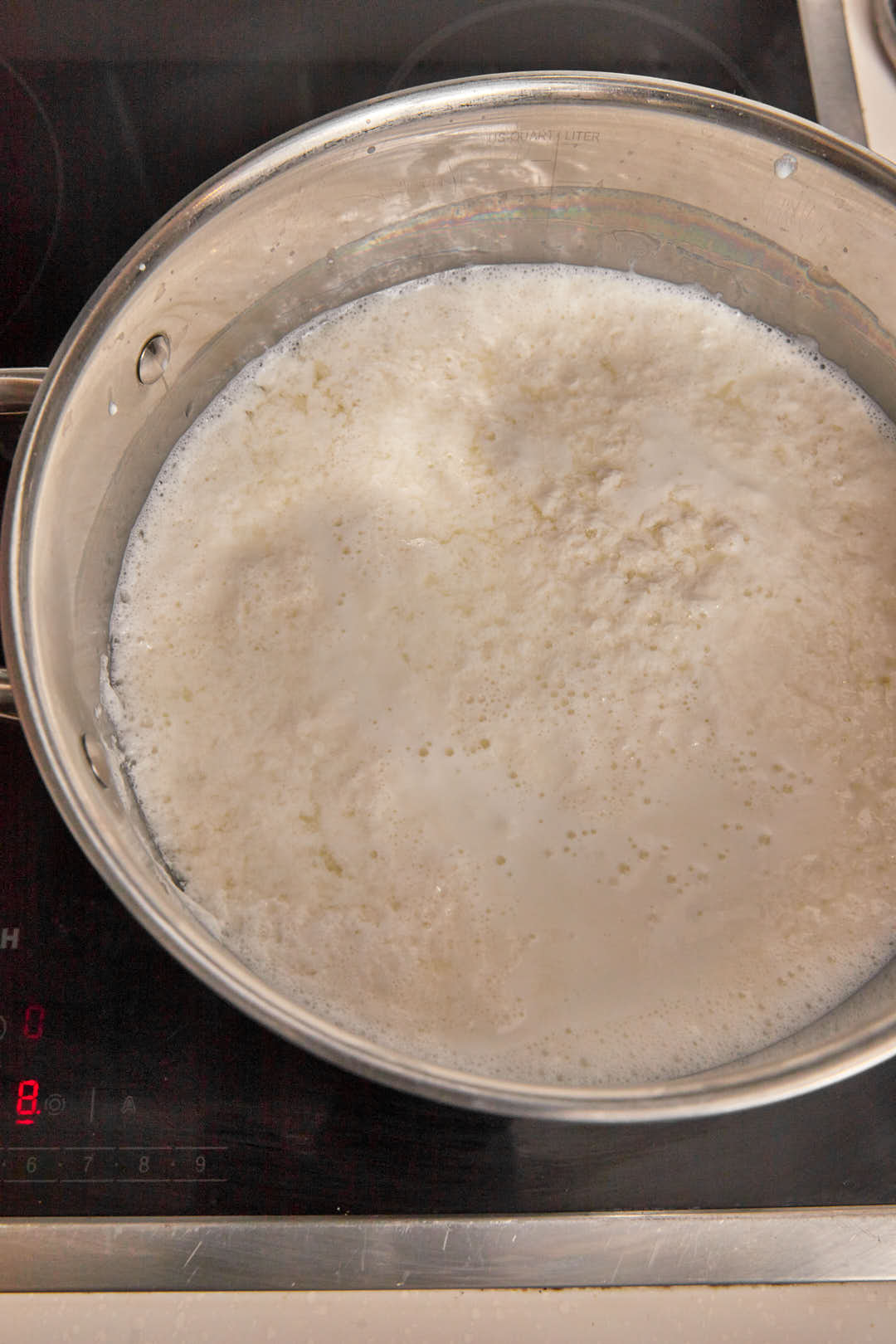 milk curds forming on the surface of a large pan of whole milk.