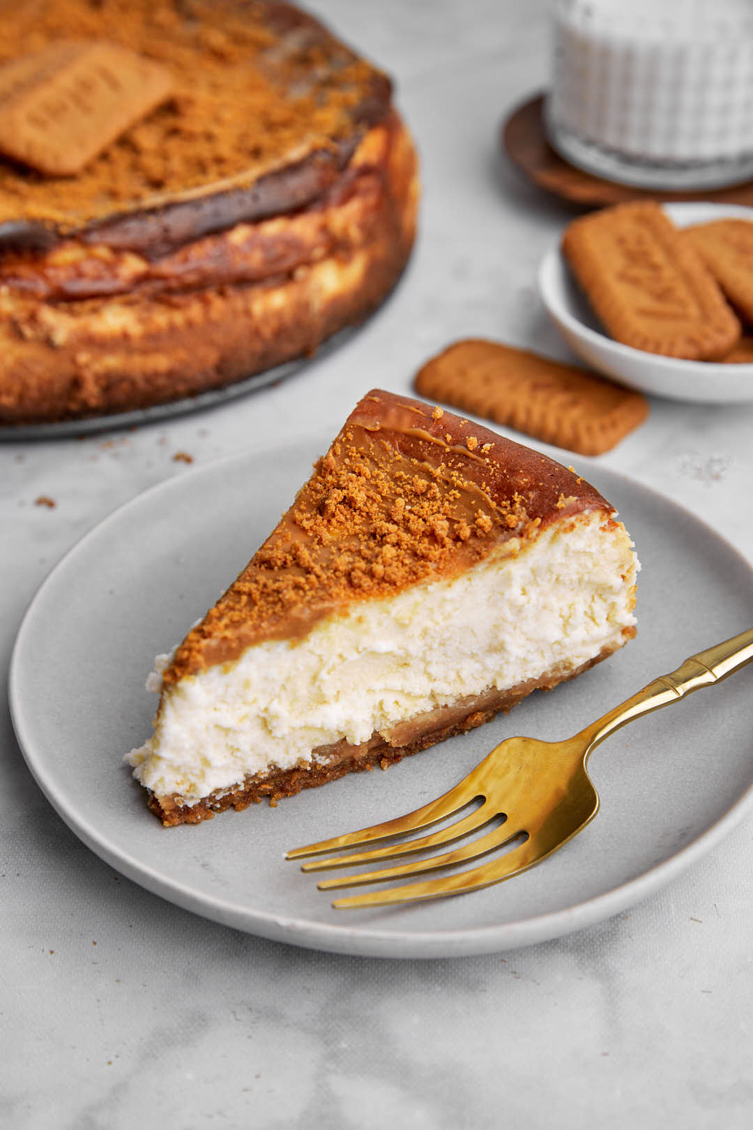 slice of cheesecake on a plate with a gold fork and biscoff biscuits in the background.