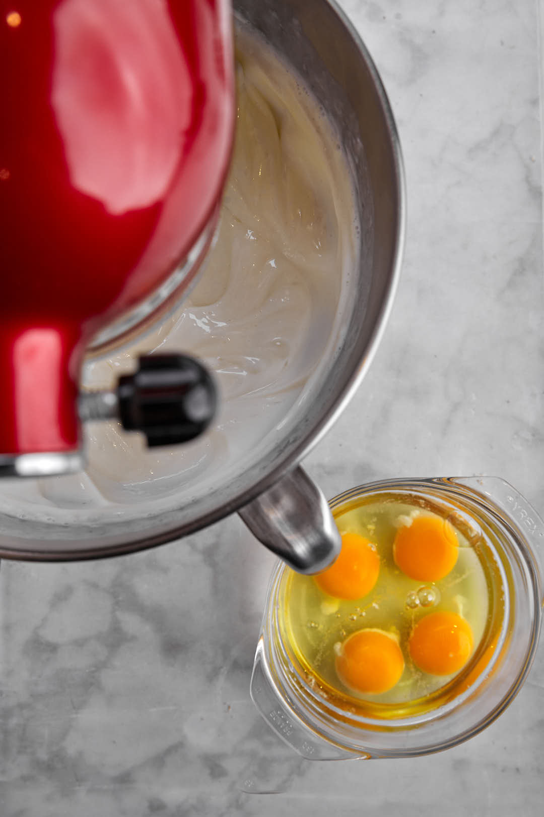 eggs in a small bowl next to a larger stand mixer bowl with cream cheese.