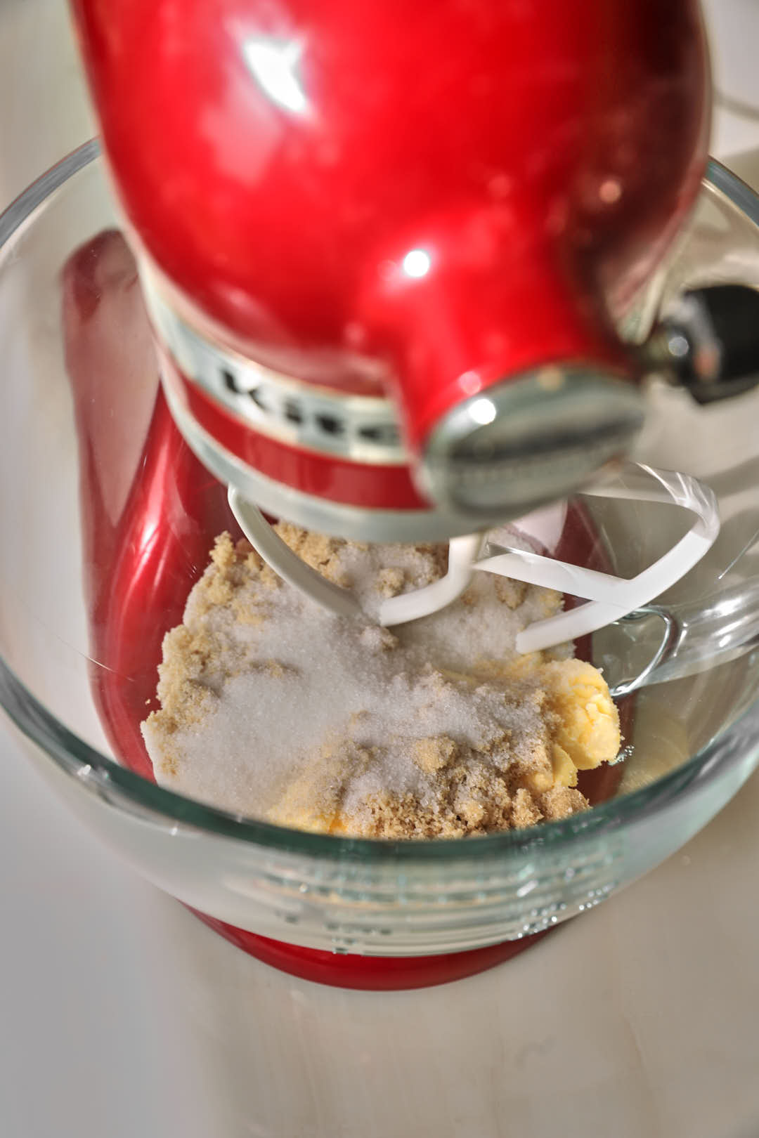 a kitchen aid with a glass bowl attached and butter, white sugar and brown sugar in the bowl.
