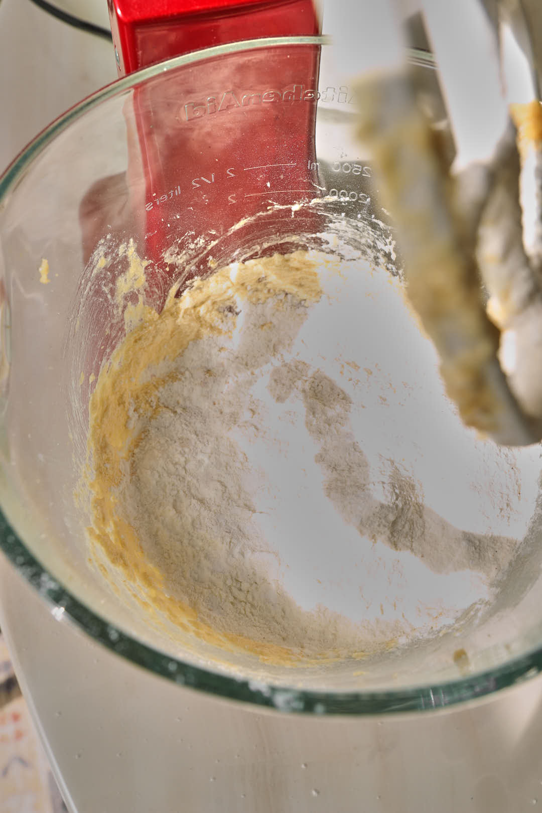 dry ingredients added to creamed butter and sugar in glass kitchen aid stand mixer bowl.