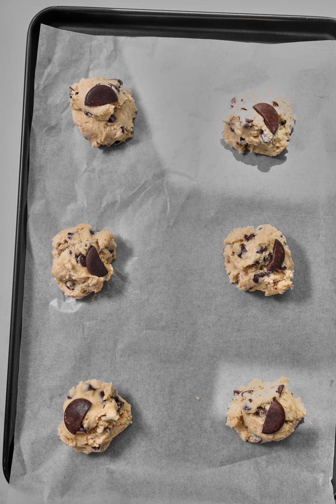 six banana chocolate chip cookie dough balls on a parchment paper lined baking sheet.
