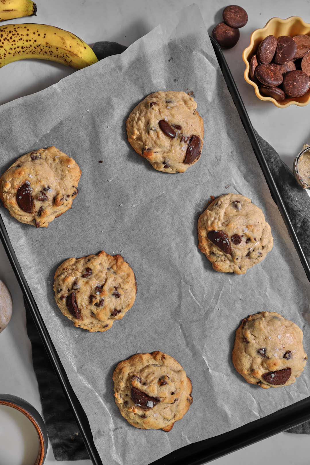 six banana chocolate chip cookies on a parchment paper lined baking sheet after baking.