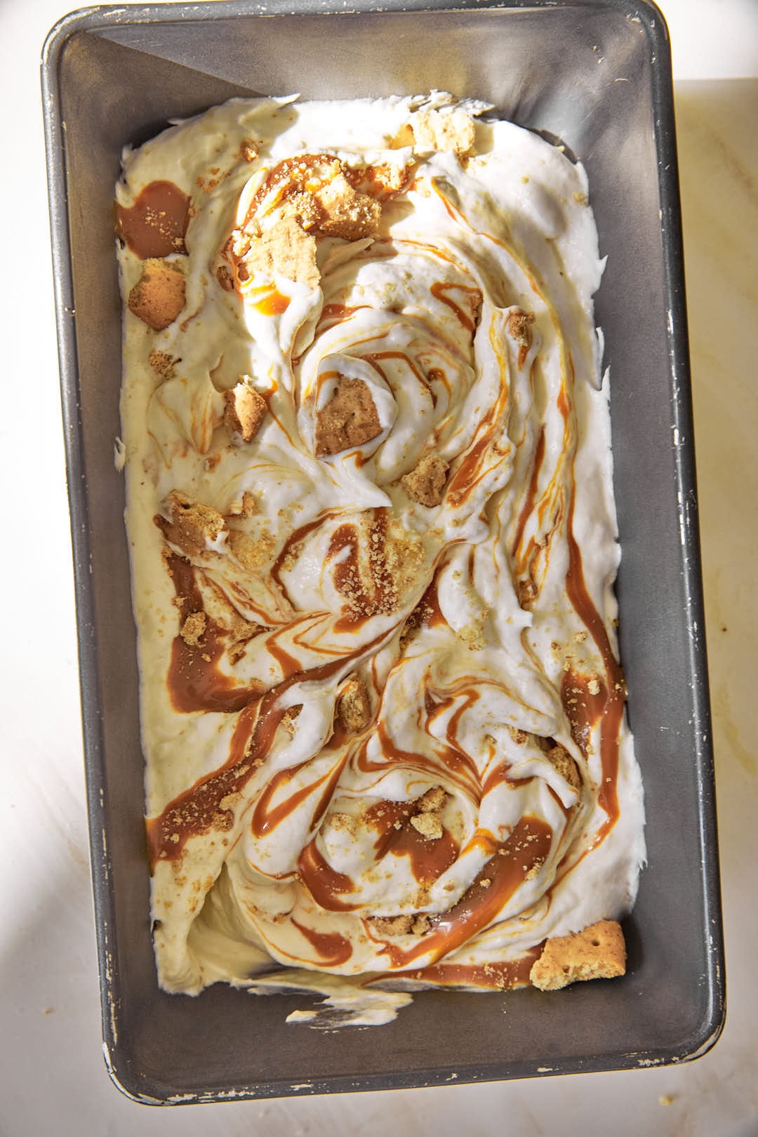 swirled toffee and biscuit pieces in banoffee ice cream in a loaf pan.