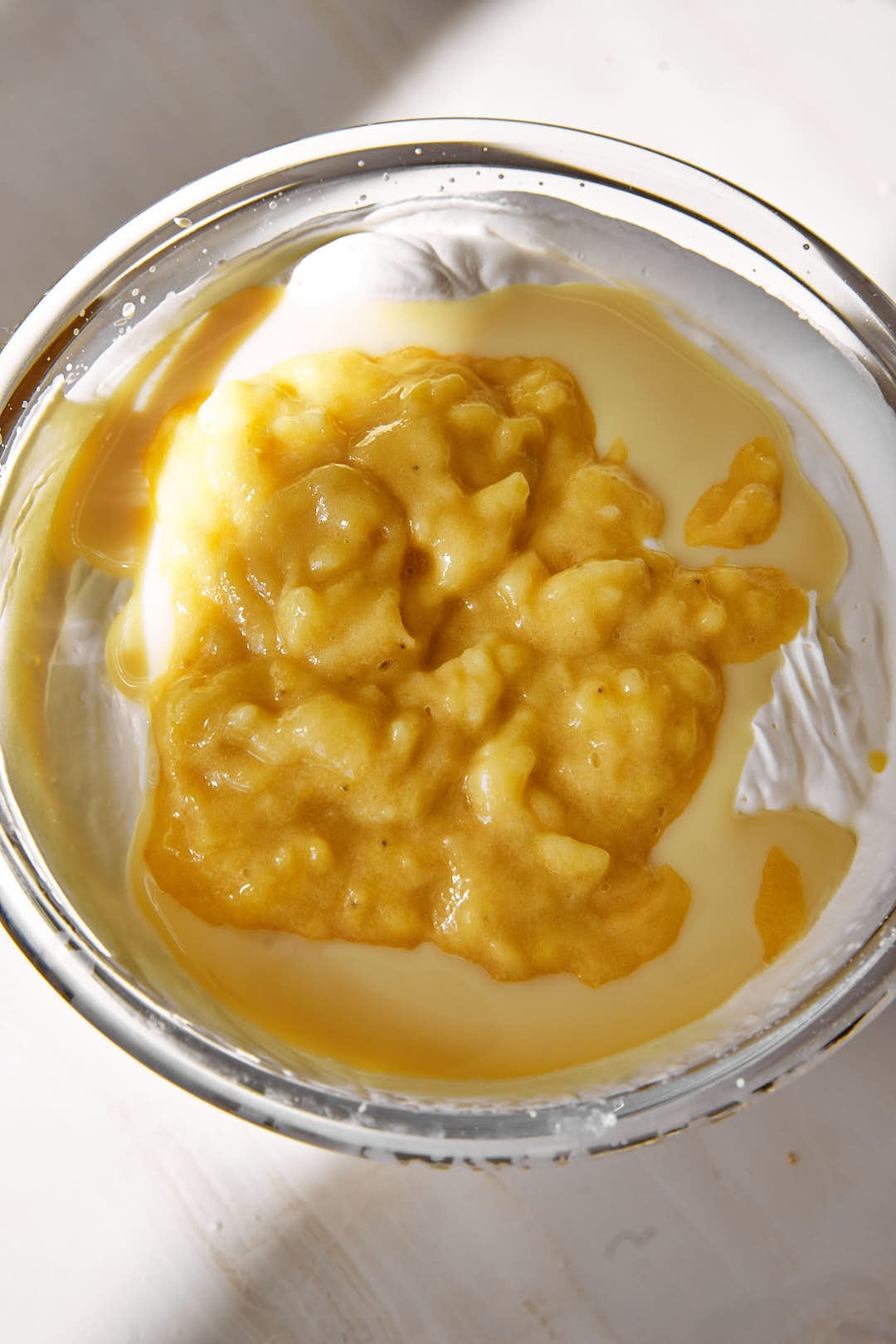 mashed bananas, condensed milk and whipped cream in a glass bowl.